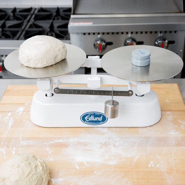 A Edlund stainless steel dough scale weighing dough on a table.
