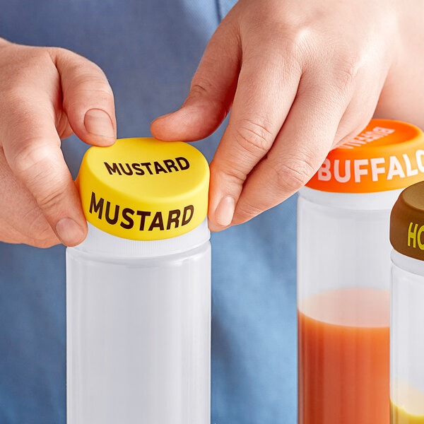 A hand holding a white squeeze bottle with a yellow cap filled with mustard.