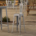 A Lancaster Table & Seating distressed nickel outdoor barstool on an outdoor patio table.