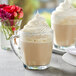 A glass mug of Capora Vanilla Latte Frappe with whipped cream on top.