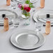 A table set with Choice silver beaded plastic charger plates, glasses, and flowers.
