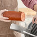 A person cutting a Prime Roots vegan Koji-salami deli stick with a meat slicer.